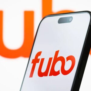 Fubo on a phone screen in front of a large Fubo logo in the background.