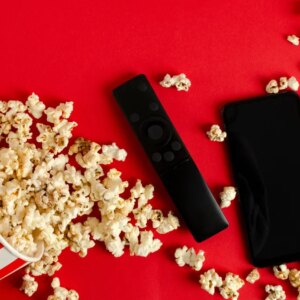 popcorn bucket, streaming remote and phone on red background
