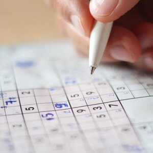 A close up of a hand with a pen filling in a Sudoku puzzle