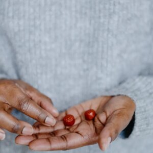A close up of a person's hand holding two red gummy supplements. They are wearing a light grey sweater.