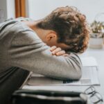 A teenage boy with his head in his arms sleeping on a book while he studies