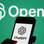 Smartphone displaying ChatGPT logo held in front of white OpenAI logo on green background
