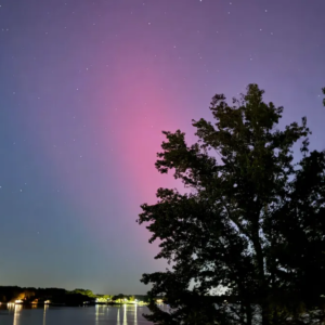 Blushing red and purple aurora over a light-lit body of water.