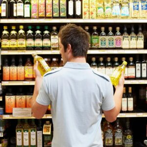 A man holding bottles of oil in a supermarket aisle.