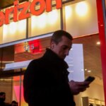 A man looking at a phone walks past a Verizon store.