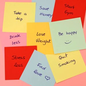 Different New Year's resolutions listed on sticky notes over a coral-colored background.