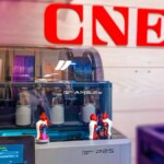 A grey printer with colored filament inside it with the CNET logo in the background