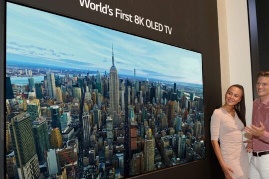 A man and woman standing next to a TV labeled the "world's first 8K OLED TV."