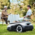 Robot lawnmower on a lawn with people in the background.
