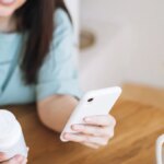 woman holding white prescription bottle in right hand and smartphone on the left hand
