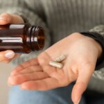 A person wearing a gray knit sweater pours beige capsules into their hand.